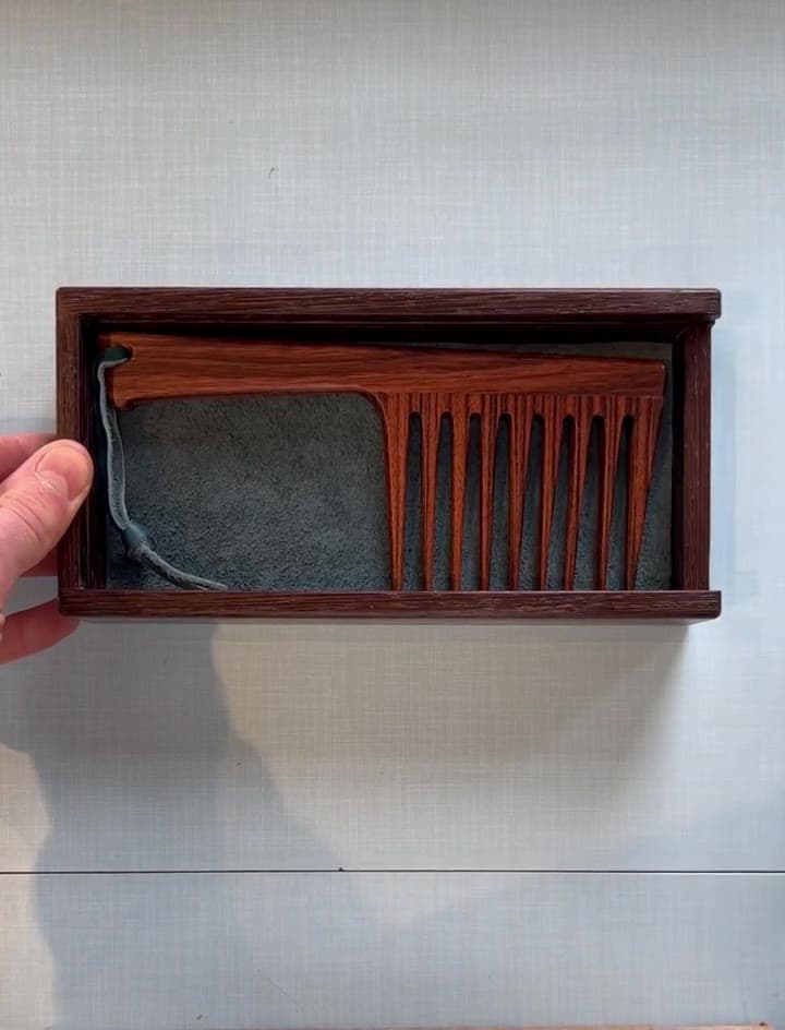 The wenge case's lid sliding off to show the tiger wood comb on grey suede
