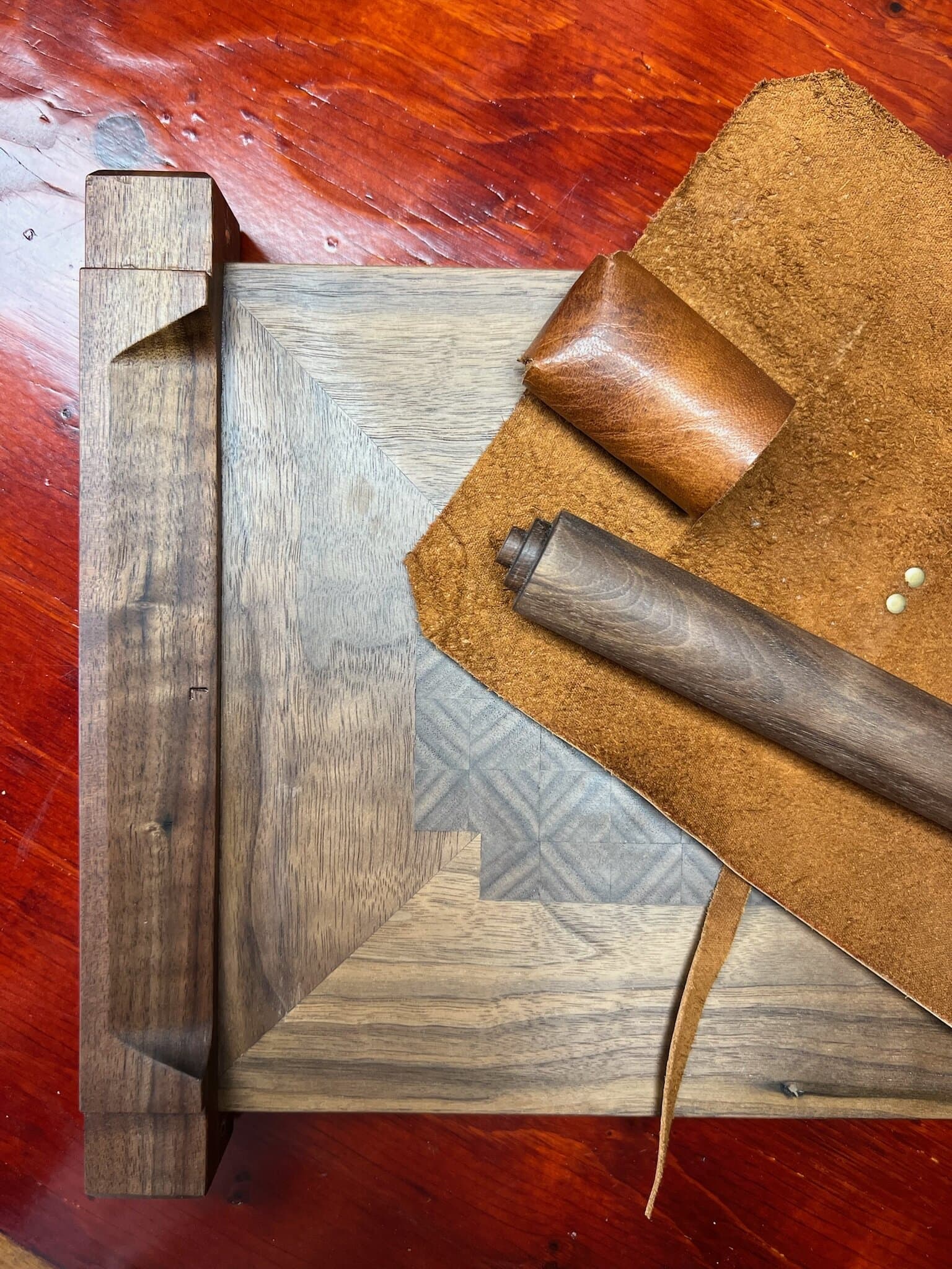 A walnut rolling pin and handle on the leather wrap, beside the chitarra