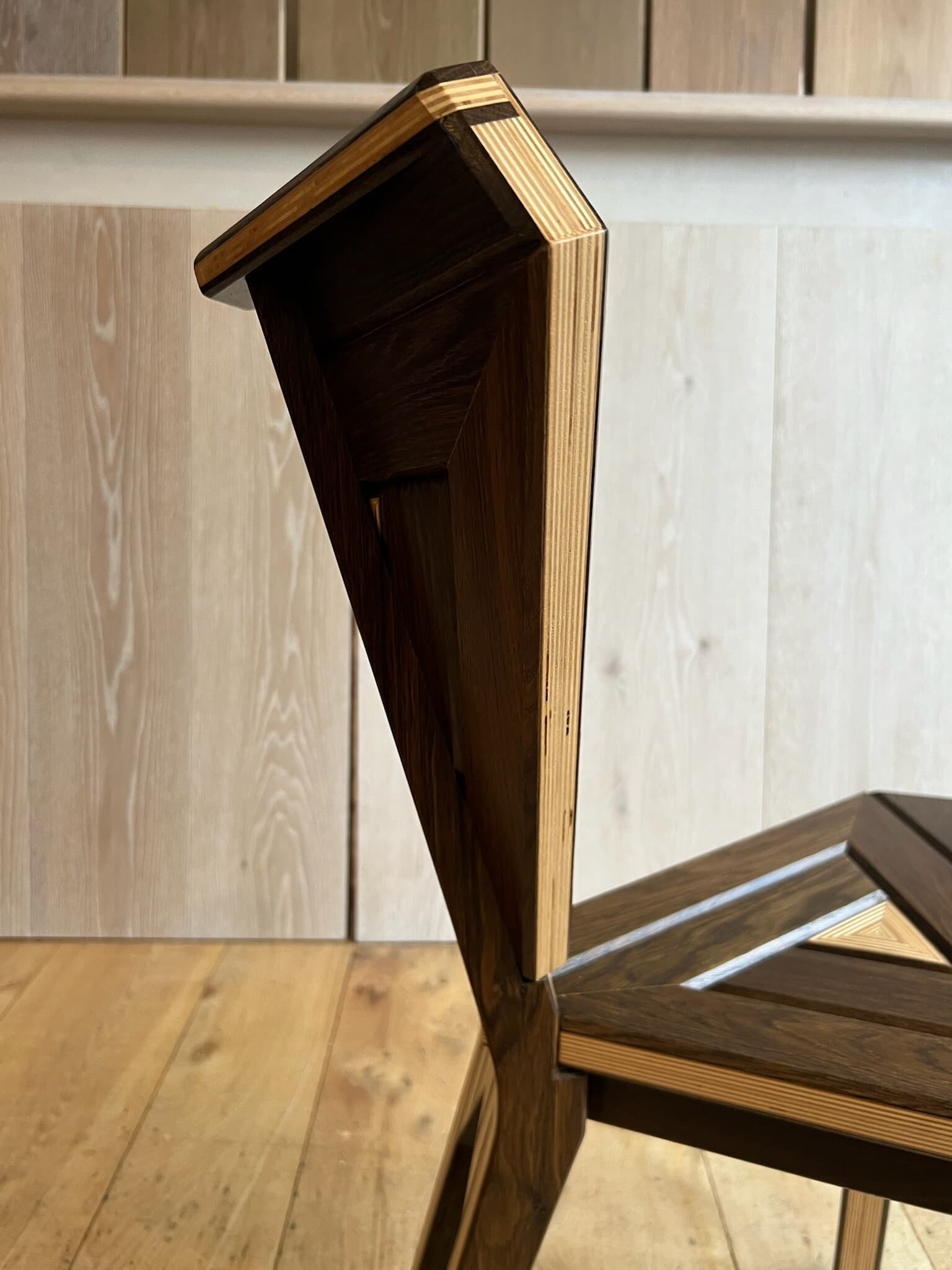 The edge of the chair's back, pale ply layers under the dark oak face