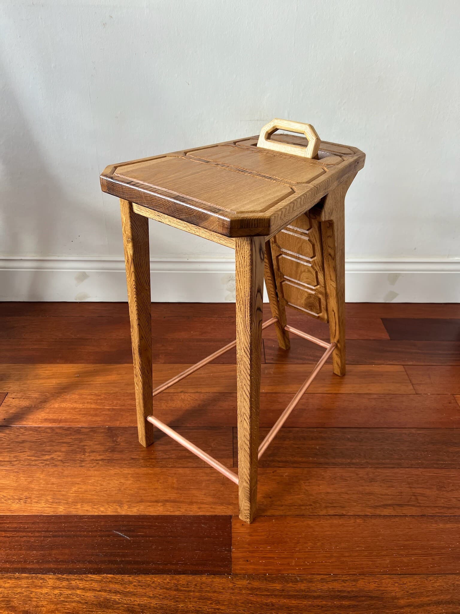 The stool with its backrest lowered, copper stretchers between the legs