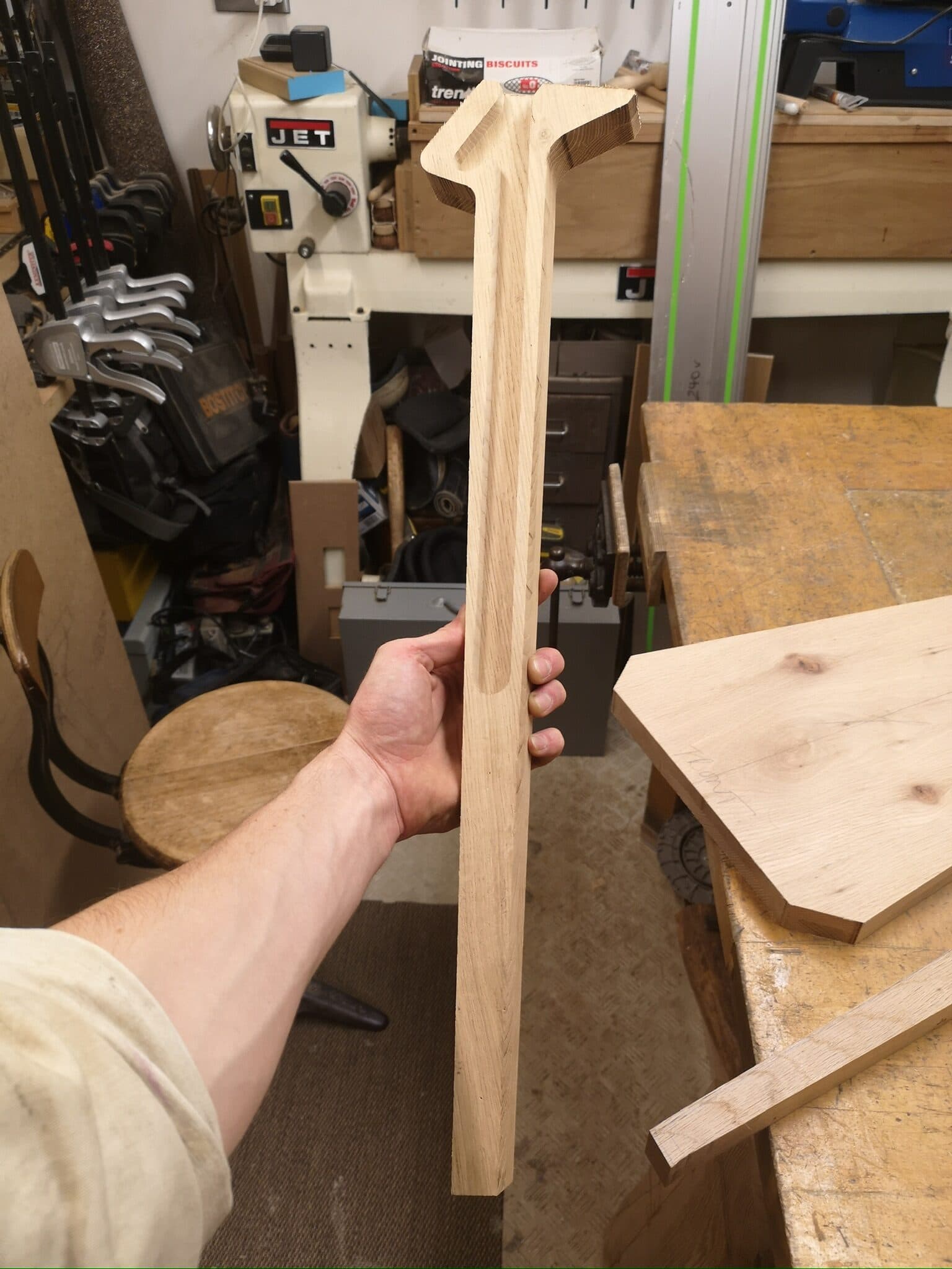 A leg blank held up against the workshop, its top already shaped